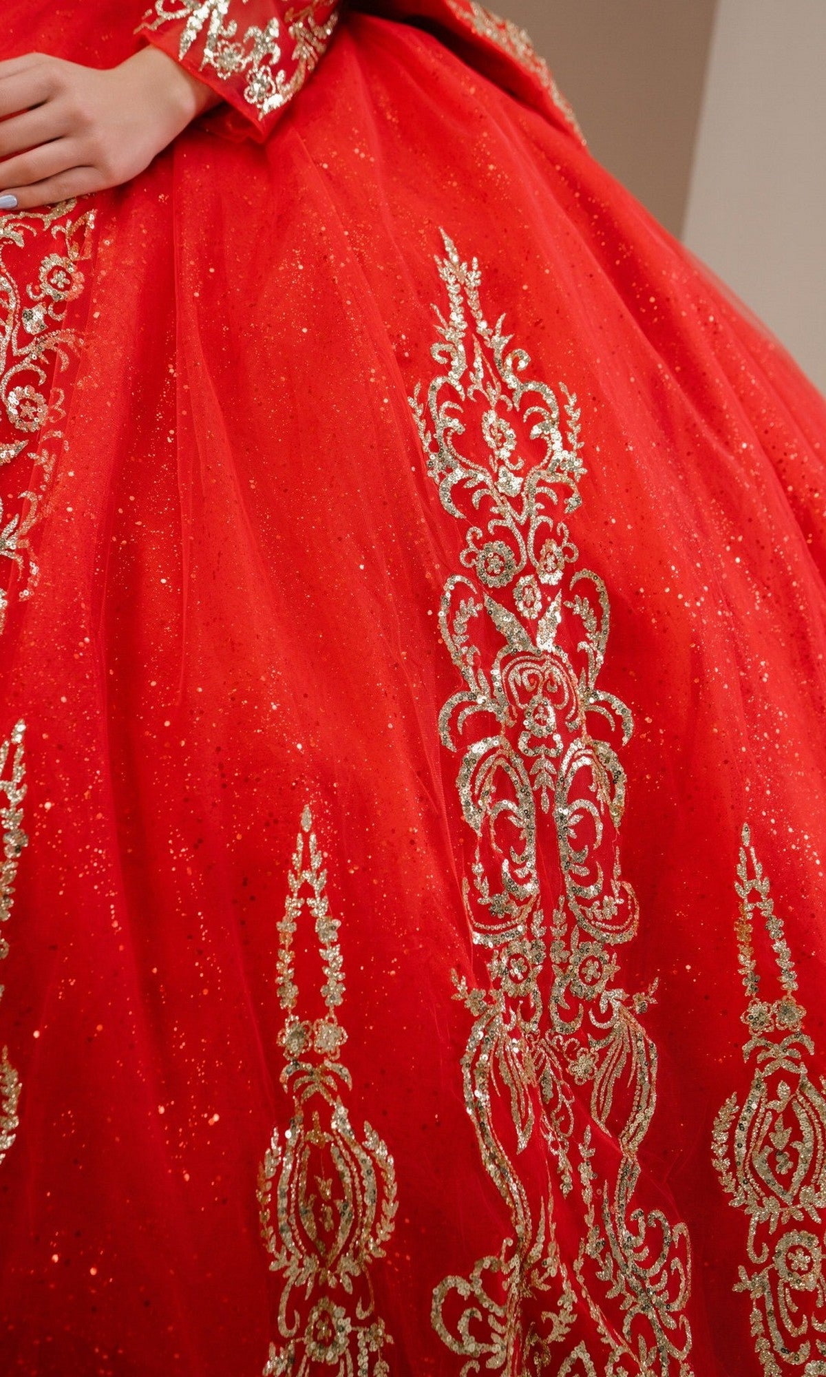 Close-up of a person wearing the Quinceanera Dress 8545JQ By Cinderella Couture, featuring a red ball gown design with intricate gold embroidery, glitter detailing, and beaded sequin embellishments.